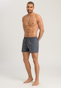 Szare szorty bokserskie w kratę z elastycznym paskiem w talii, z zapięciem na guziki i swobodnym krojem. Materiał wydaje się lekki i oddychający.