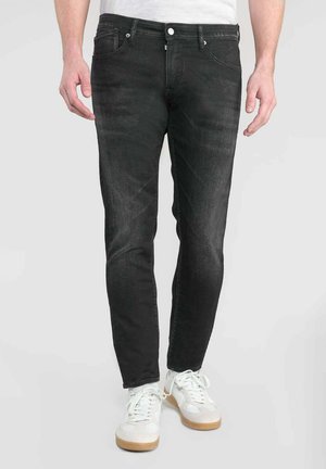 Jeans de mezclilla negros con un corte ajustado, diseño de cinco bolsillos, cierre frontal con botón y desgaste sutil; llevados con zapatillas blancas.