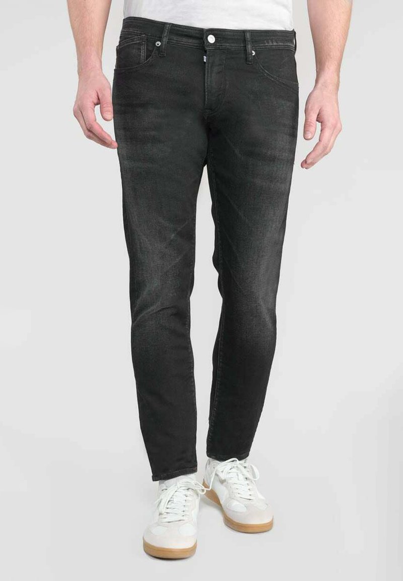 Jeans de mezclilla negros con un corte ajustado, diseño de cinco bolsillos, cierre frontal con botón y desgaste sutil; llevados con zapatillas blancas.