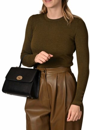Femme portant un haut à manches longues vert olive et un pantalon en cuir marron, tenant un sac à main noir avec une fermeture dorée dans sa main gauche.