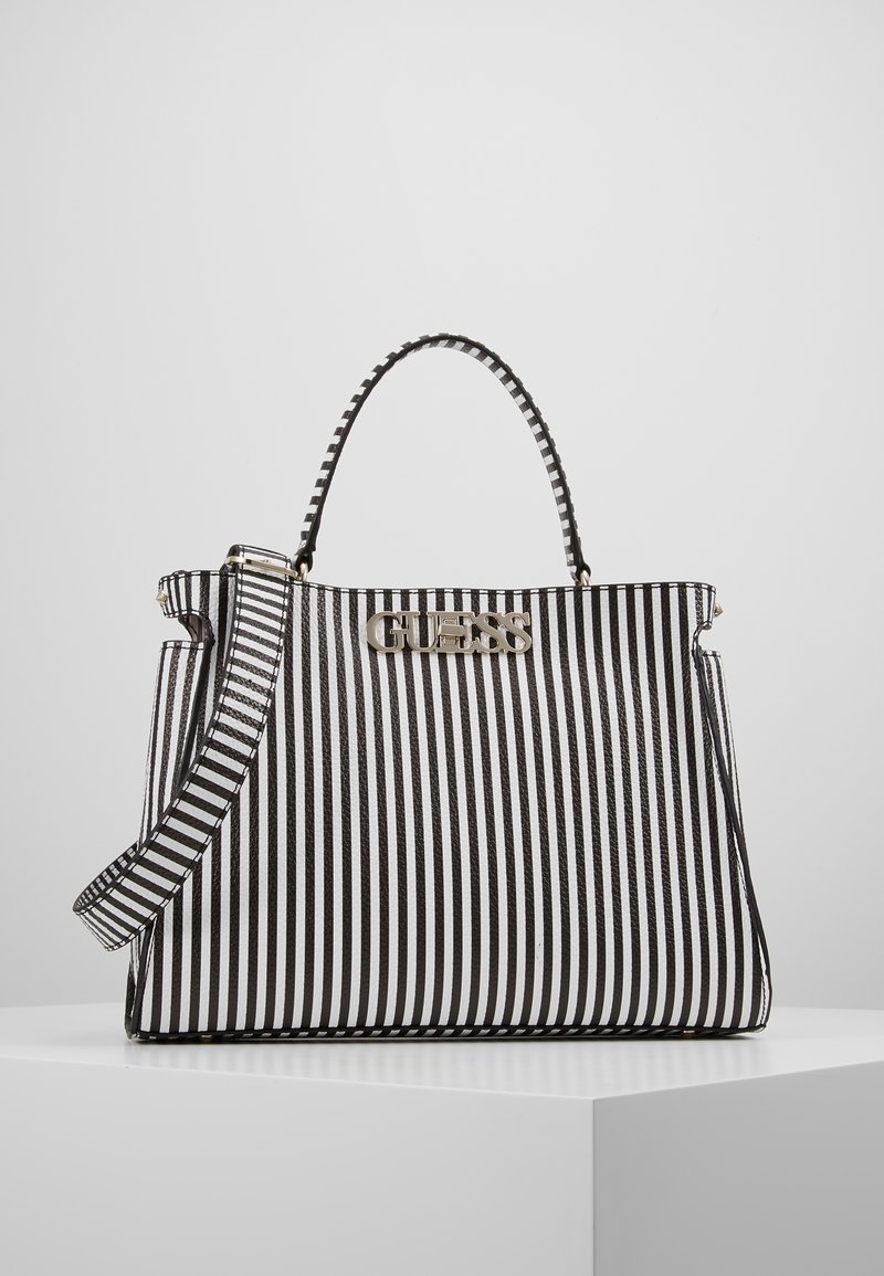 Sac à main à rayures verticales noires et blanches avec une poignée supérieure, une bandoulière réglable et un logo doré "GUESS" sur le devant.