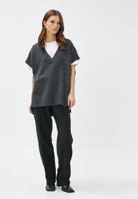 Grijze gebreide poncho trui met een V-hals, korte mouwen en ribgebreide hemden, gelaagd over een witte blouse. Gecombineerd met zwarte smalle broeken.