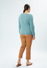 Lyseblå, fluffy striktrøje med lange ærmer; parret med tanfarvede, tapered bukser med optrukket kant og brune flade sandaler.