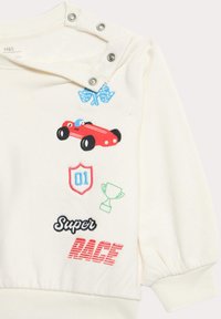 Cremefarbener Fleece-Pullover mit gestickten Patches in Form eines Autos, eines Schildes, eines Pokals und Text. Mit Druckknopfverschluss an der Schulter und gerippten Bündchen.