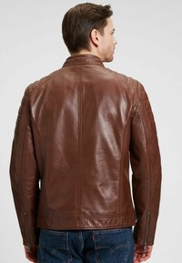 Chaqueta de cuero marrón con una textura suave, diseño ajustado y acentos acolchados en los hombros. Presenta puños con cremallera y un cuello clásico.