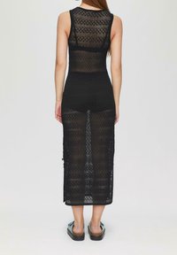 Musta neulottu mekko, jossa on hihaton malli, pitsikuvioita ja nilkkoihin ulottuva pitkä leikkaus. Yhdistetty litteiden sandaalien kanssa.