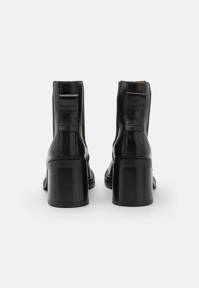 Botas de tobillo de cuero negro con tacón cuadrado, paneles laterales elásticos y detalles de logo grabado en la parte trasera. Acabado suave y brillante.