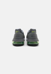 Zapatillas Nike con una parte superior de malla gris, amortiguación de aire verde y una suela negra en contraste. Los acentos incluyen un detalle del logotipo amarillo.