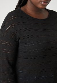 Μαύρο πλεκτό πουλόβερ με οριζόντιες γραμμές από ανοιχτές πλέξεις. Στρογγυλή λαιμόκοψη και μακριά μανίκια, με υφή.