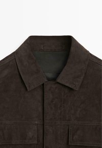 Giacca in camoscio marrone con colletto classico, chiusura frontale con bottoni e due tasche sul petto. Presenta una texture morbida e dettagli di cuciture pulite.