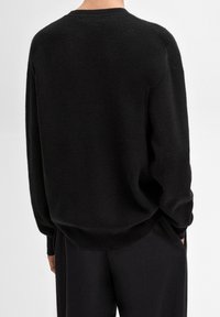 Czarny sweter dzianinowy o luźnym kroju, z teksturowaną powierzchnią i okrągłym dekoltem. Długie rękawy sięgają nadgarstków.