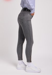 Jeans ajustados grises de cintura alta, con un acento de cremallera en el tobillo, cinco bolsillos y una tela ligeramente elástica para un look ceñido.