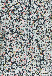 Bluse mit floralem Muster in Schwarz, Creme und Rot, mit einem Knopf-Frontdesign. Das Material wirkt leicht und hat eine angenehme Textur.