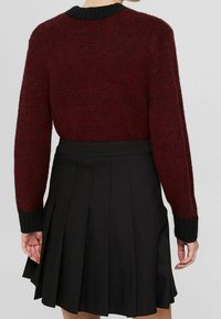 Pull en maille bordeaux texturé avec des poignets et un col noir, associé à une jupe plissée noire. Vue de dos montrant les détails du vêtement.