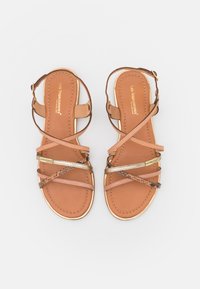 Bruine leren sandalen met meerdere gekruiste banden in lichtroze en gouden accenten, voorzien van een gevoerde zool en een platte zool.