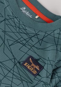 Türkiser Pullover mit einem grafischen Muster aus dunkelgrünen Linien. Verfügt über einen orangefarbenen Kragen und einen Stoffpatch mit einem Fuchs-Logo.