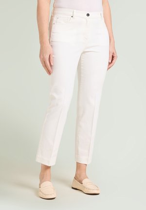 Pantalones blancos ajustados de pierna recta combinados con mocasines beige, mostrados en una persona de pie sobre un fondo pálido.