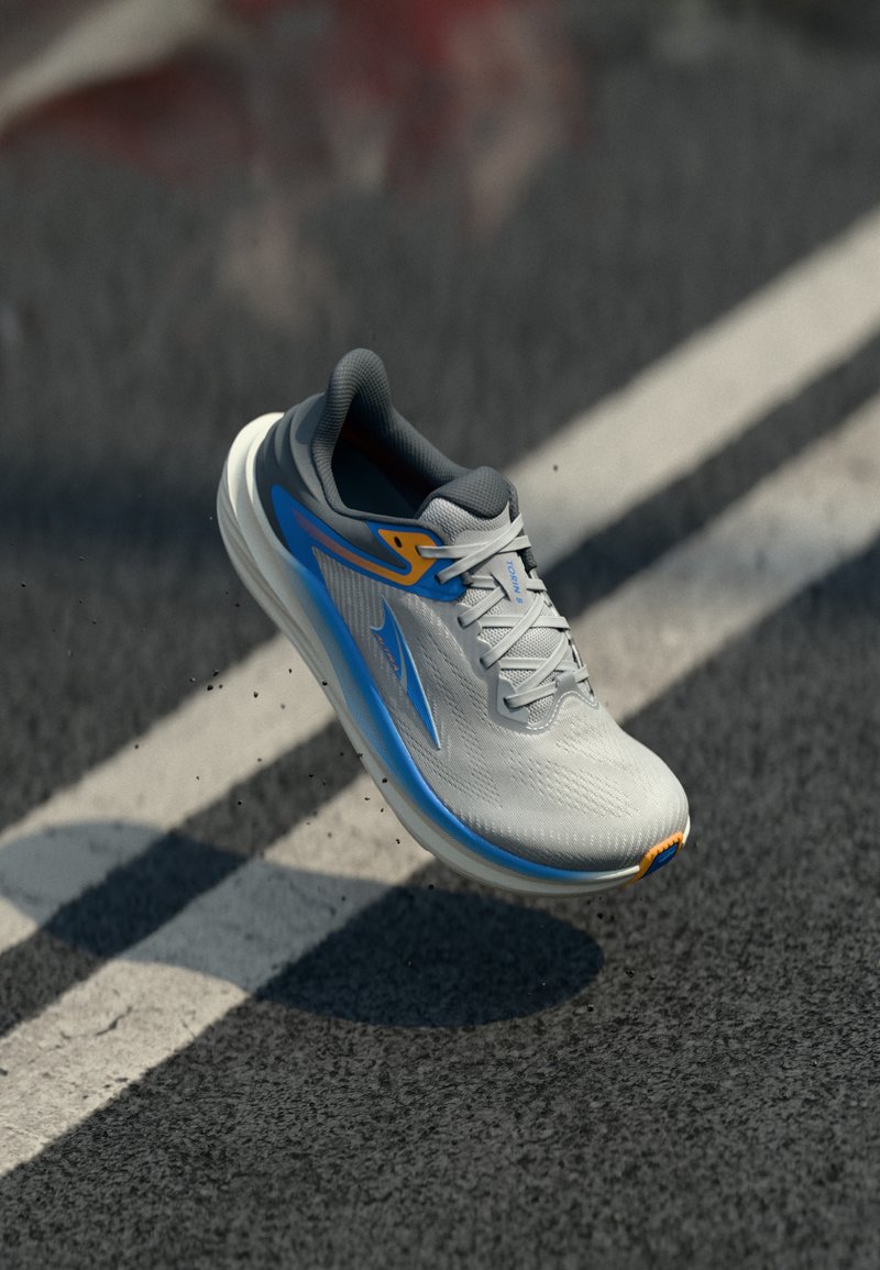Ανοιχτό γκρι και μπλε παπούτσι για τρέξιμο στον αέρα πάνω από ασφαλτο με λευκές λωρίδες δρόμου, που δείχνει τη σόλα και κίνηση ταχύτητας με μικρά σωματίδια βρωμιάς.