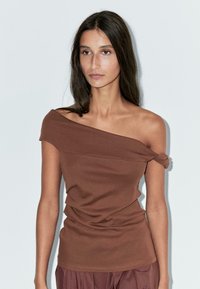 Top marrone, scollato sulle spalle, realizzato in tessuto morbido con dettaglio a nodo su una manica e texture drappeggiata lungo il corpo, design aderente.