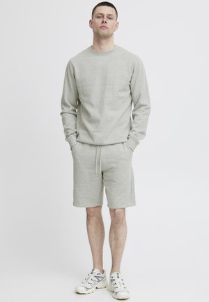Grå sweatshirt og matchende shorts lavet af blødt stof, med en afslappet pasform, rund halsudskæring og snøre i taljen. Hvide sneakers.