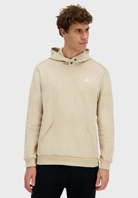 Sudadera con capucha beige de tela suave, con un bolsillo tipo canguro, detalles de botones falsos en el cuello y un pequeño logo en el pecho.