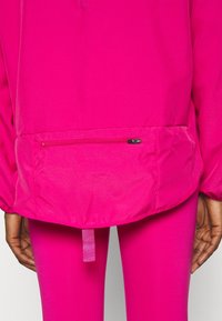 Jasnoróżowa, rozpinana kurtka z kieszenią na zamek z tyłu, elastycznymi mankietami i pasem. Gładka tekstura, odpowiednia do odzieży sportowej.