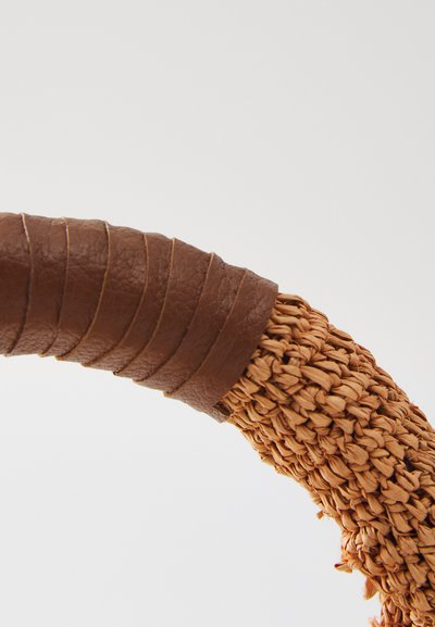 Vevd kurvhandling med teksturerte naturfibre, pakket inn i glatt brun lær, med en buet, ergonomisk form.