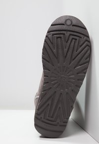 Šedá semišová podrážka boty s diamantovým vzorem běhounu, uprostřed s kruhovým logem a texturovaným povrchem pro lepší přilnavost.