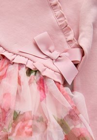 Indumento rosa con una parte superiore texturizzata e bordi arricciati, decorato con un nastro rosa e un sovrapposto in tulle a fantasia floreale nella parte inferiore.