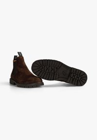 Botas Chelsea de ante marrón con paneles laterales elásticos y tirador. Suela de goma gruesa con tacos para una mejor tracción.