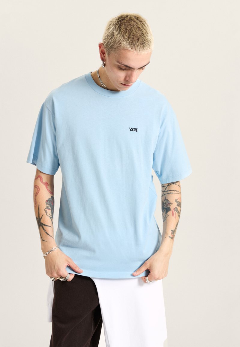Světle modré bavlněné tričko s černým logem Vans na hrudi, krátké rukávy a volný střih.
