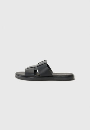 Black slide sandals featuring two crossed straps, smooth leather texture, and a flat sole. Simple design with no additional embellishments.