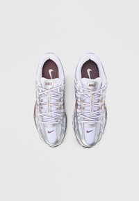 Άσπρα αθλητικά παπούτσια Nike με μεταλλική ασημί επικάλυψη, υφή από δίχτυ στο επάνω μέρος, μωβ λεπτομέρειες και ανακλαστικά κορδόνια. Λογότυπο στη γλώσσα και στο πλάι.