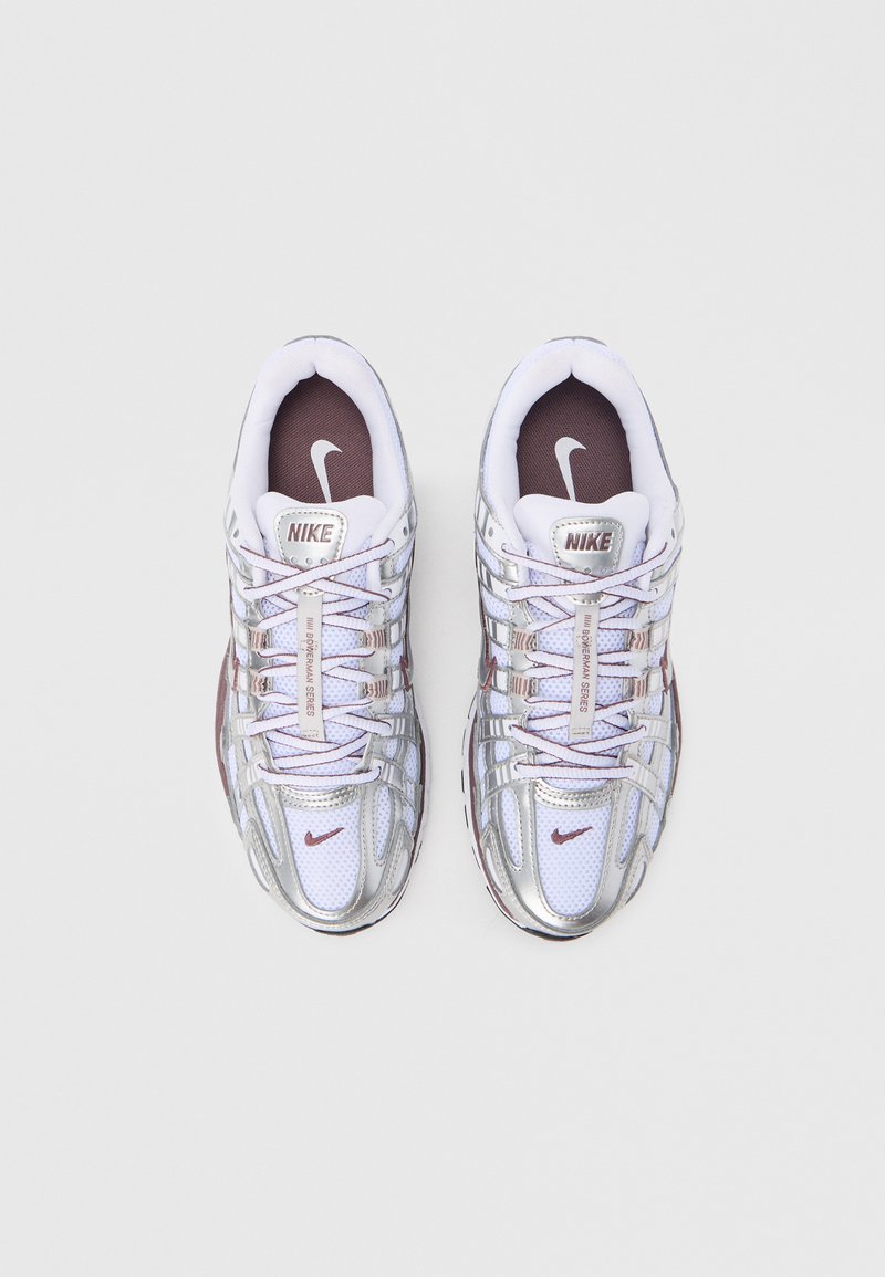 Baskets blanches Nike avec une superposition argentée métallique, tige en mesh texturé, accents violets et lacets réfléchissants. Logo sur la languette et le côté.