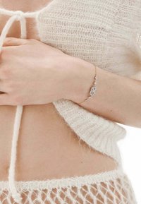 Pulsera de oro con un diseño geométrico que presenta formas rectangulares y de diamante, adornada con patrones intrincados, llevada en un tono de piel claro.