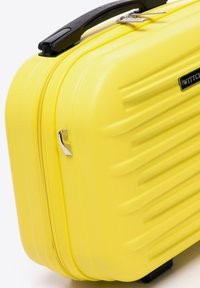 Maleta rígida de color amarillo brillante, con textura acanalada, cierre de cremallera y un asa negra con un acento plateado para un transporte fácil.
