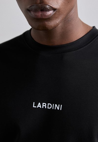 Melna t-krekls ar apaļu kakla izgriezumu, izgatavots no gludas auduma, ar zīmola nosaukumu "LARDINI" baltā krāsā priekšā.