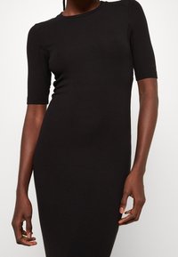 Robe noire côtelée à manches courtes, au design ajusté, avec un col rond et une texture lisse. Aucun motif ou détail en métal visible.