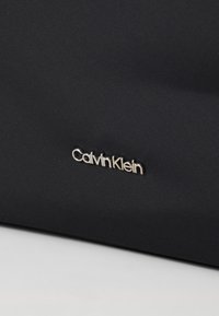Borsa in tessuto nero con texture, accentuata dal logo argentato "Calvin Klein". Presenta un design elegante e uno stile minimalista.