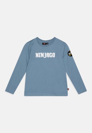 Majica dugih rukava plave boje od pamuka s bijelim natpisom "NINJAGO" sprijeda i okruglim izrezom s crnom zakrpom na rukavu.