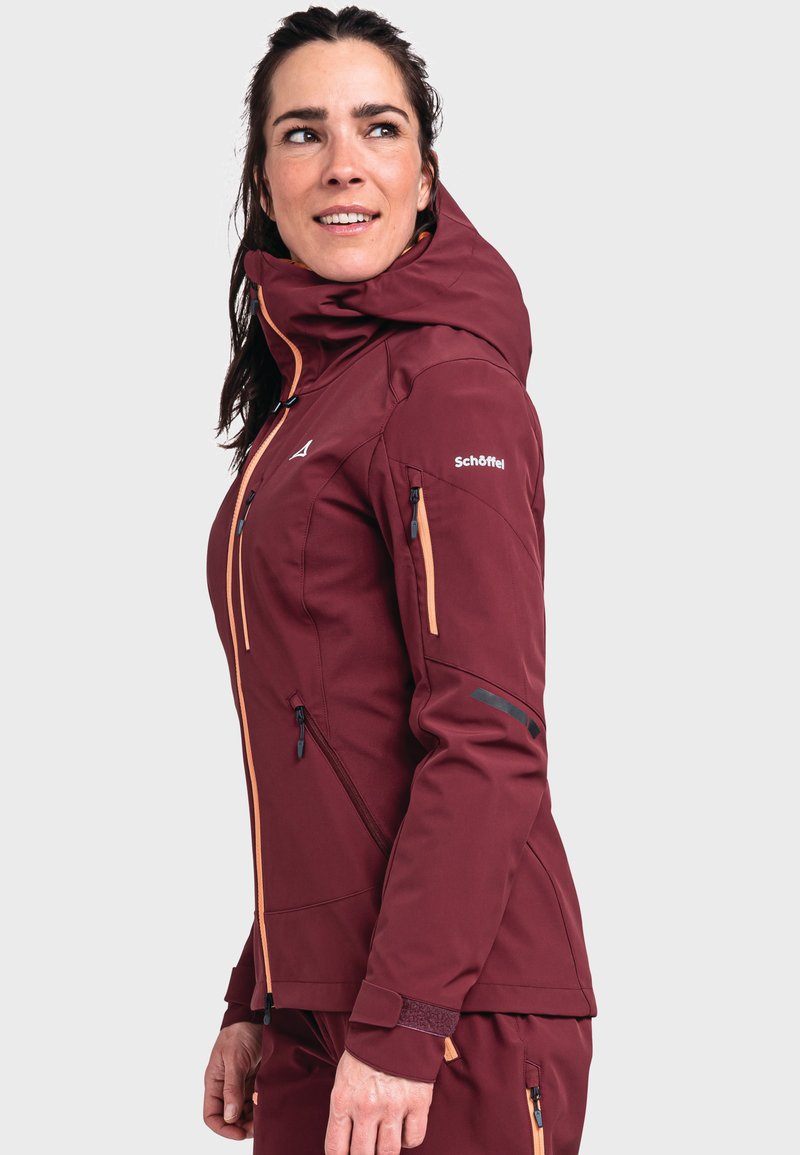 Burgunderrote Softshell-Jacke mit orangefarbenen Reißverschlüssen, verstellbarem Kapuzenkragen, Seitentaschen und eng anliegenden Bündchen. Sie verfügt über ein schlankes, konturiertes Design für optimale Beweglichkeit.