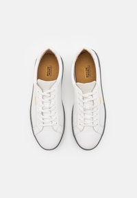 Weiße Leder-Sneaker mit runder Zehenpartie, flacher grauer Gummisohle und klassischem Schnürdesign. Minimalistische Markenkennzeichnung und glatte Textur.