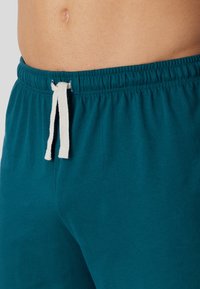 Teal cotton shorts with an elastic waistband, featuring a contrasting white drawstring for adjustment. Smooth texture with minimal detailing.