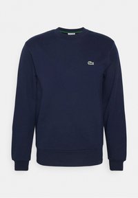 Sweat-shirt bleu marine col rond en coton, doté de manches longues et d'un petit logo Lacoste vert sur le côté gauche de la poitrine. Couleur unie avec des poignets côtelés.