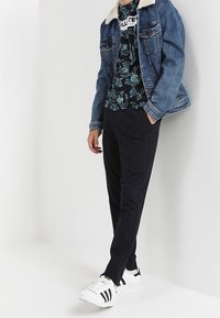 Jeansjacka med en vit fårskinnskrage, svart blommig T-shirt och svarta byxor, kompletterad med vita sneakers med svarta ränder.