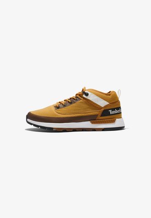 Zapatilla Timberland marrón y amarilla con suela blanca y negra, cierre de cordones en la parte delantera y parche con marca en el talón, mostrada de perfil.