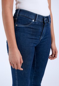 Dark blue denim jeans with a fitted design, featuring front pockets, belt loops, and light stitching accents along the seams.