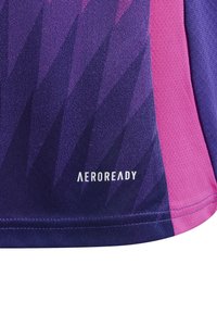 Fioletowa koszulka sportowa z trójkątnym wzorem w różnych odcieniach, z różowymi akcentami. Na dole widoczny napis "AEROREADY".