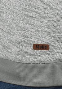 Grå teksturert genser med ribbestrikket kant. Har et brunt lærmerke med "iSolid"-merket. Mykt, strikket stoff med et lett mønster.