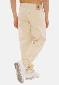 Cremfarbene, locker sitzende Hosen mit doppelten Gesäßtaschen und einem gestickten Markenlabel an der Taille. Tragen Sie dazu weiße Sneakers.